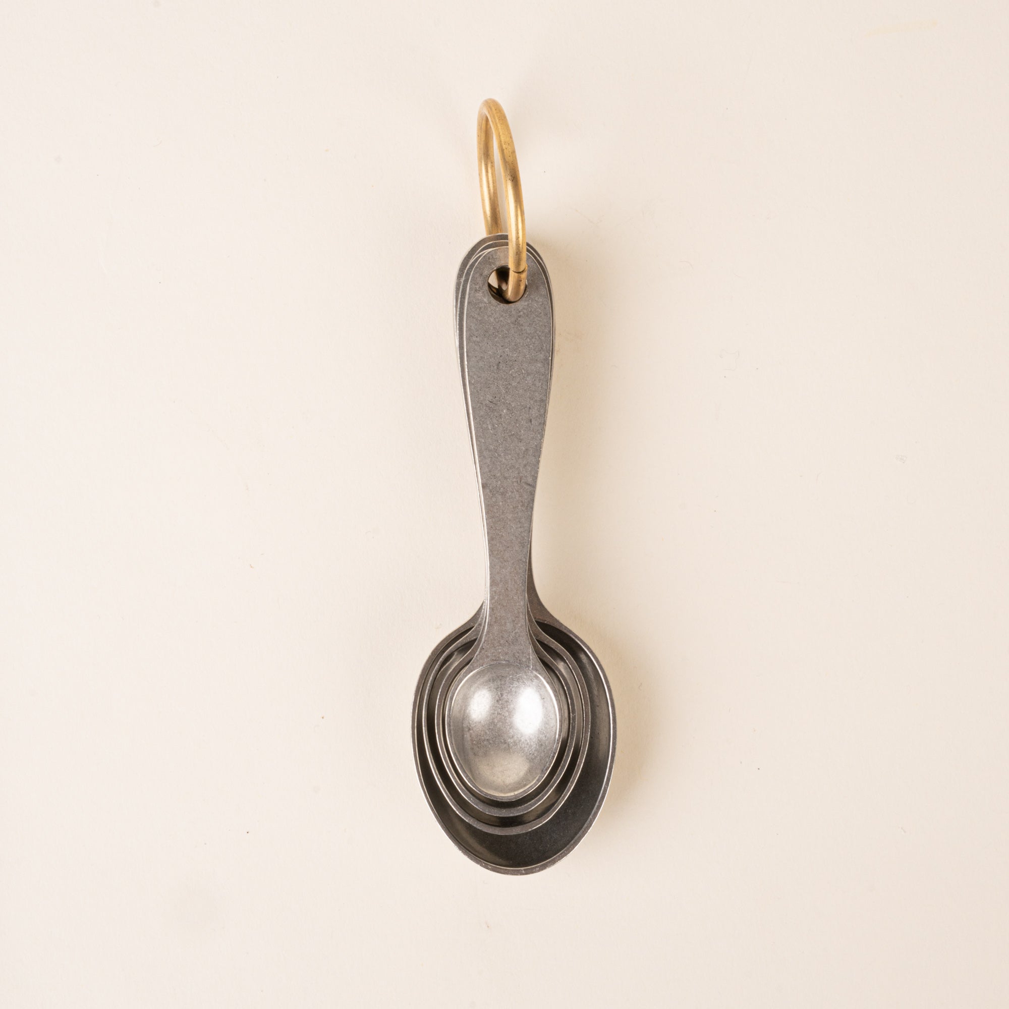 Four pewter measuring spoons on a brass ring, nested together.