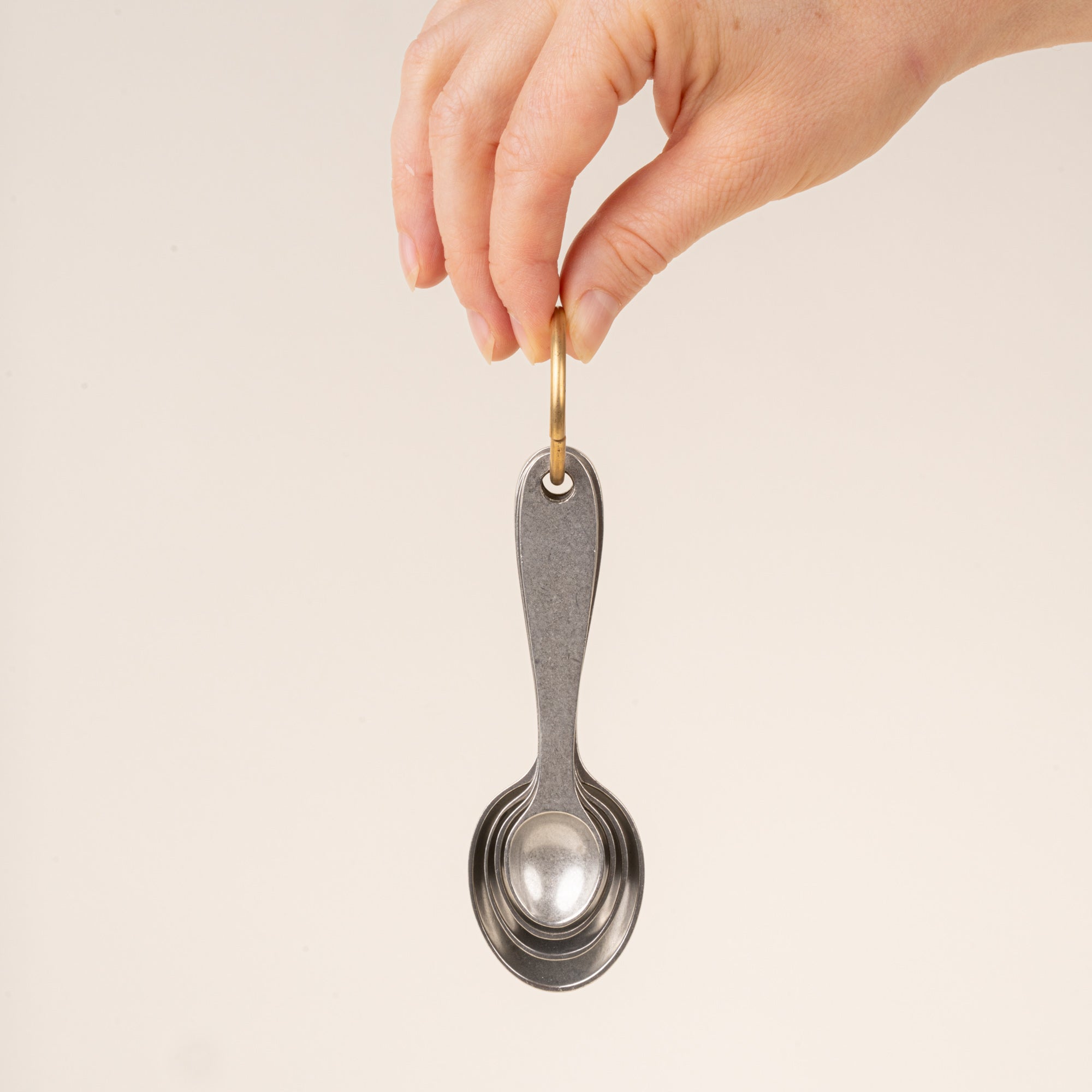 A hand holds four pewter measuring spoons on a brass ring nested together.