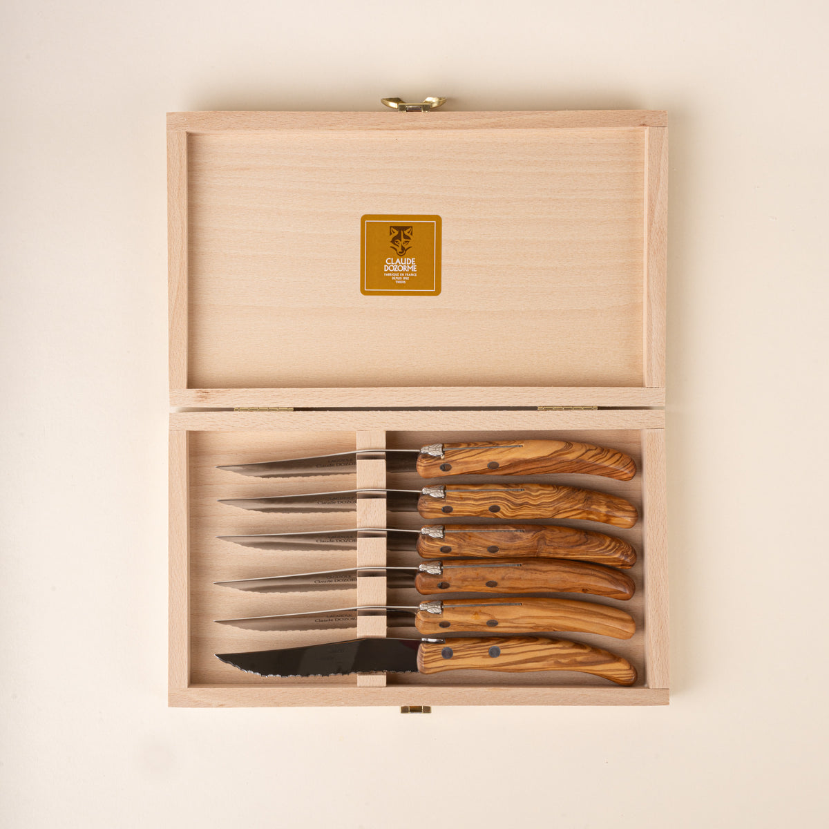 Set of six steak knives with polished steel blades and richly grained olive wood handles, sitting in a rectangular wooden box.