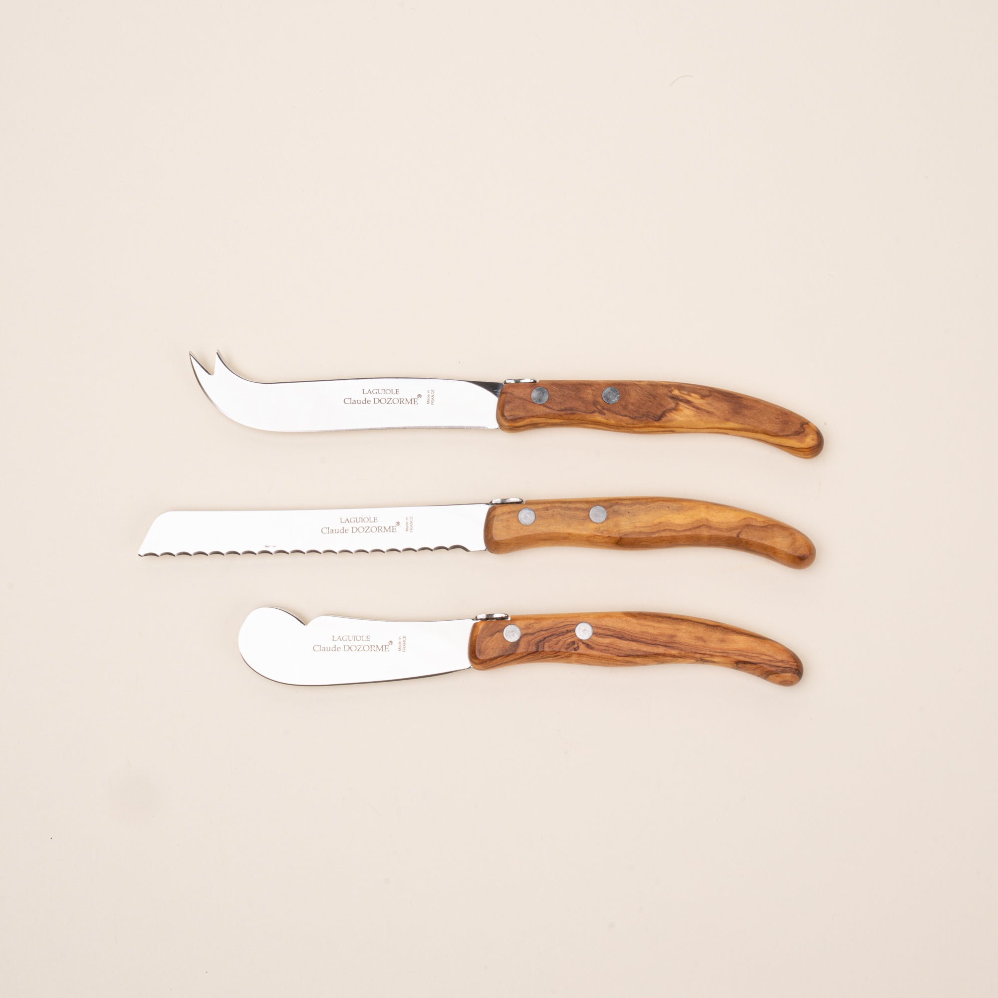 Set of three serving knives with polished steel blades and olive wood handles, including cheese, bread, and spreader knives.