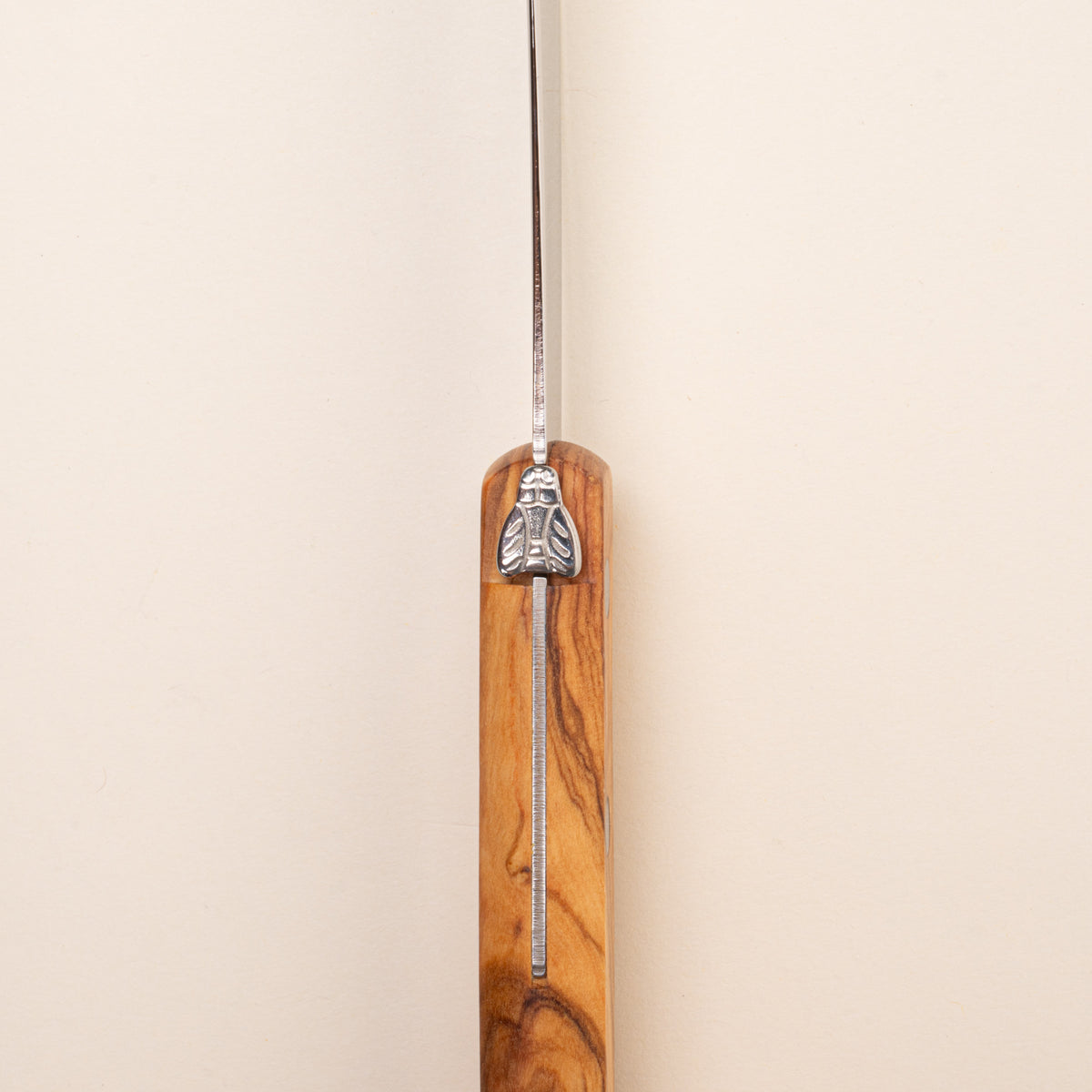 A close-up of a knife with a polished wooden handle and a silver metal blade, featuring a decorative silver bee emblem near the bolster.