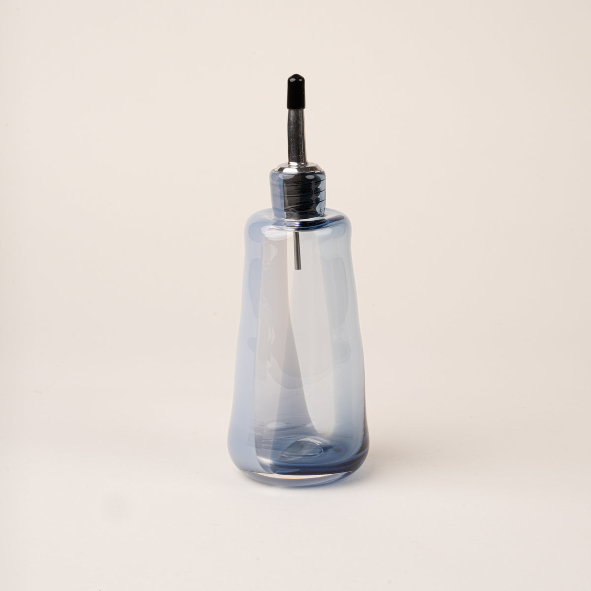 A blue-gray glass oil or vinegar dispenser with a polished metal pour spout and stopper.