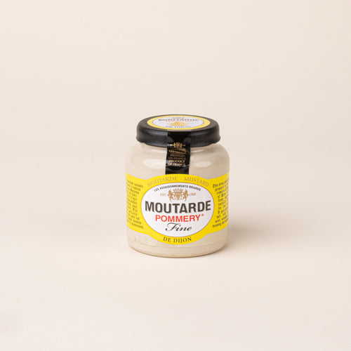 Glass jar of Pommery Fine Dijon mustard with a black lid and yellow and white label on a cream background.