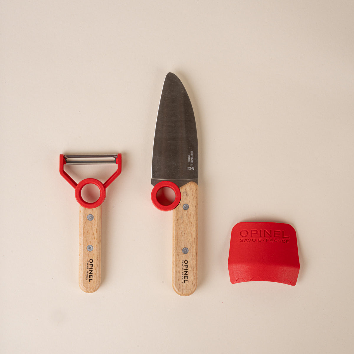 Kitchen tool set for children with a peeler, chef’s knife, and red scraper, each with red accents.