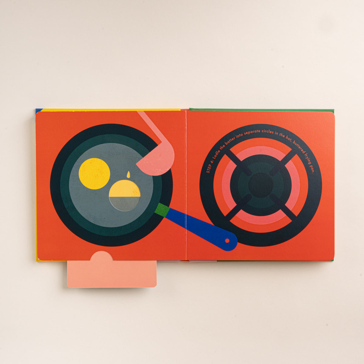 Open interactive pancake recipe book showing batter being poured into a frying pan beside an illustrated stovetop burner.