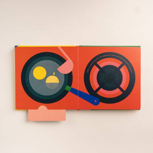 Open interactive pancake recipe book showing batter being poured into a frying pan beside an illustrated stovetop burner.