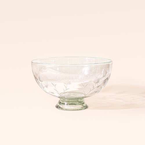 A larger clear glass footed bowl with etched floral designs, on a cream background.