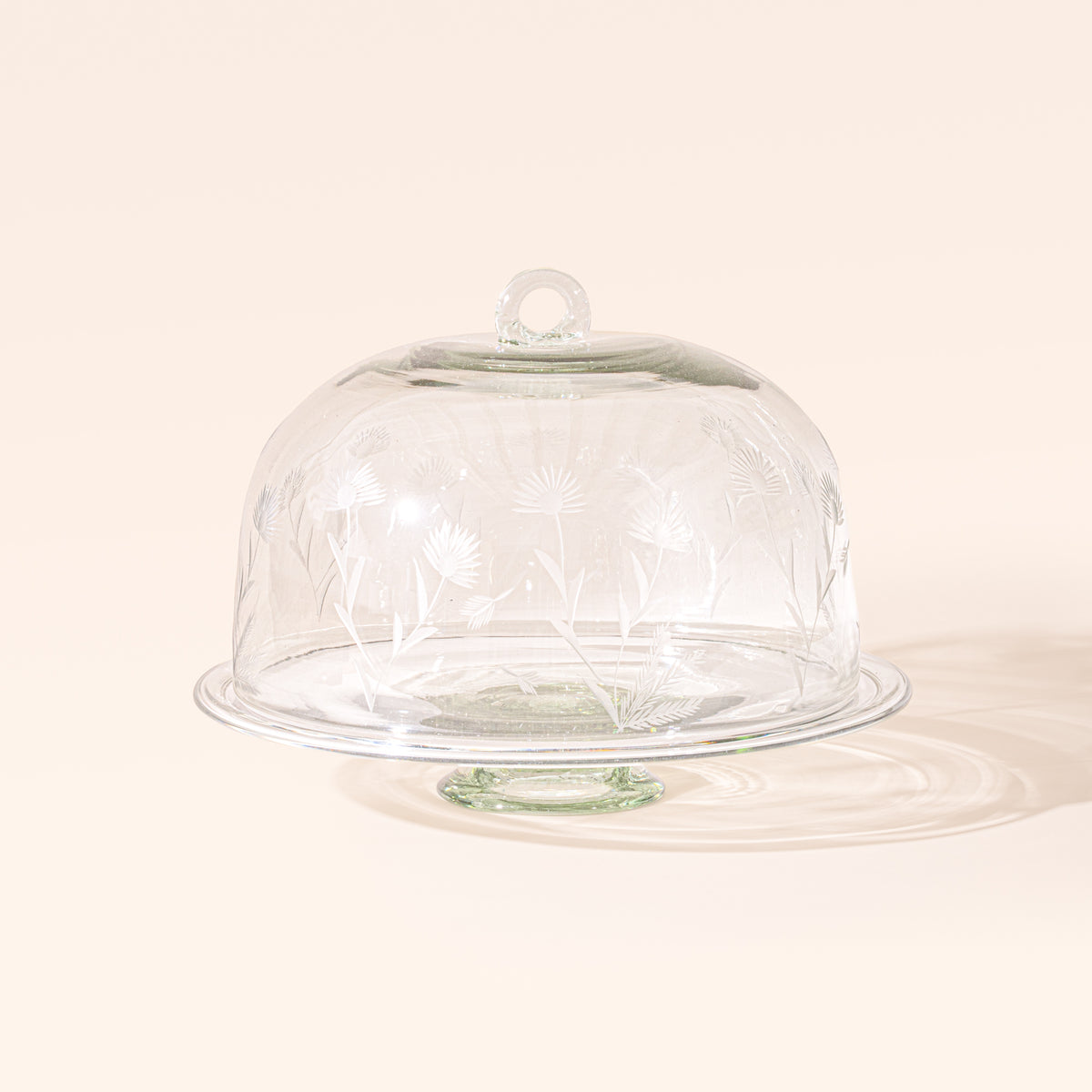 An etched floral glass dome on a clear glass cake stand.