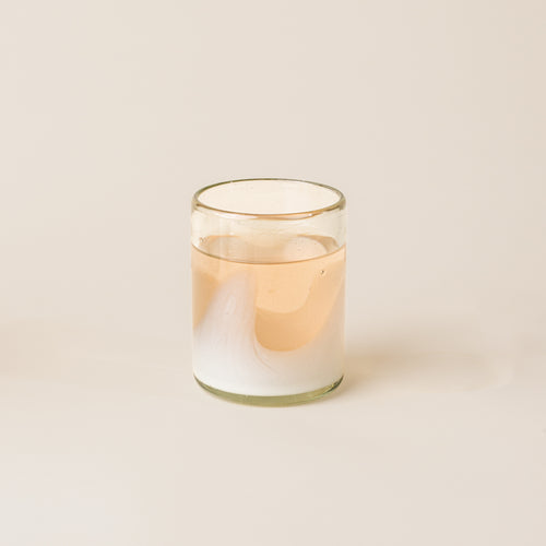 A white and clear handblown glass tumbler with organic wave design, filled with a pink lemonade drink.