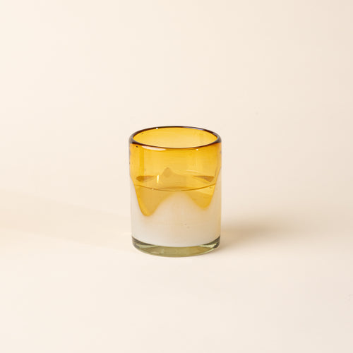 Water in an amber and clear handblown glass tumbler with organic wave design, casting a soft golden shadow on a beige backdrop.
