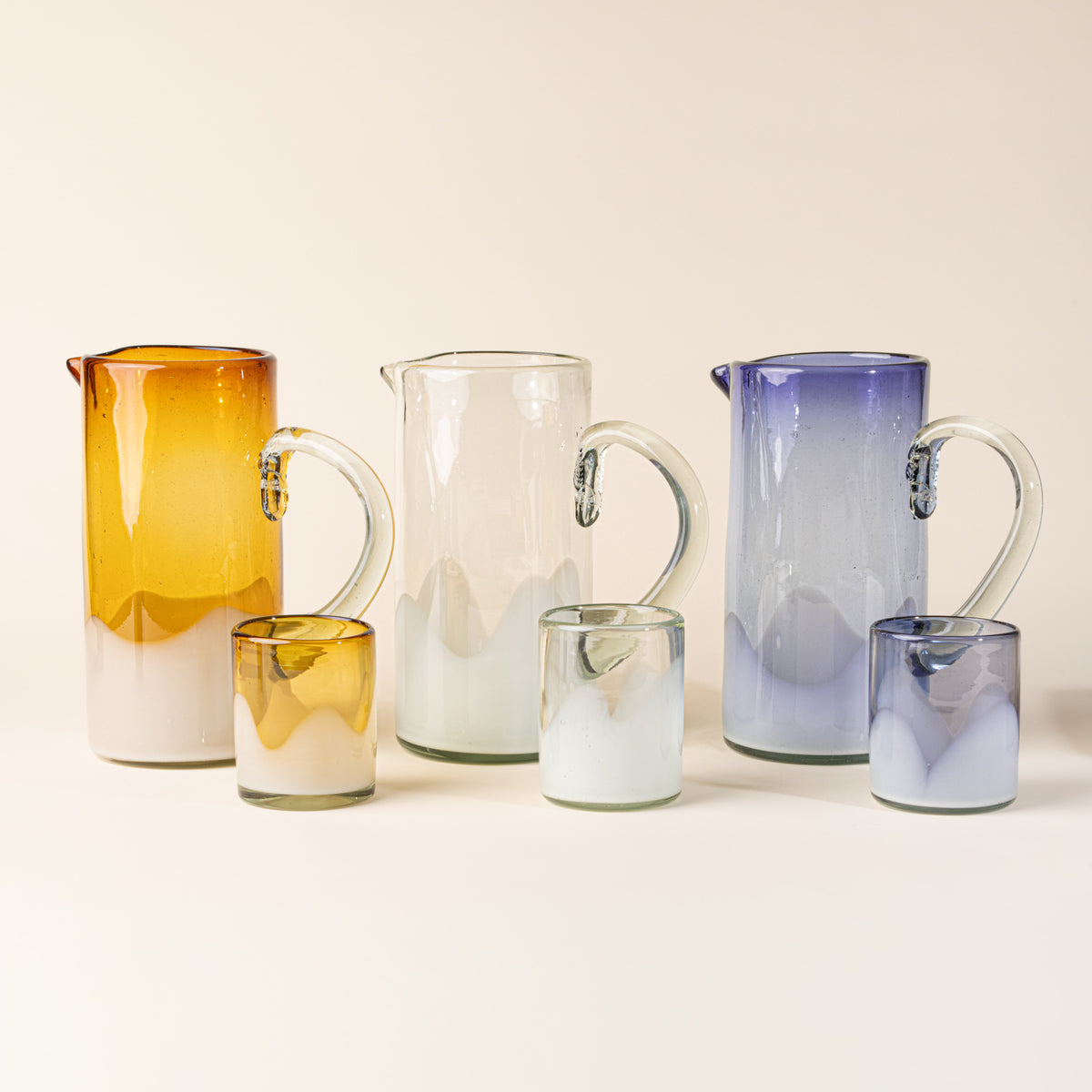 Three glass pitchers and matching tumblers in amber, clear, and violet with white wavy dipped bases.