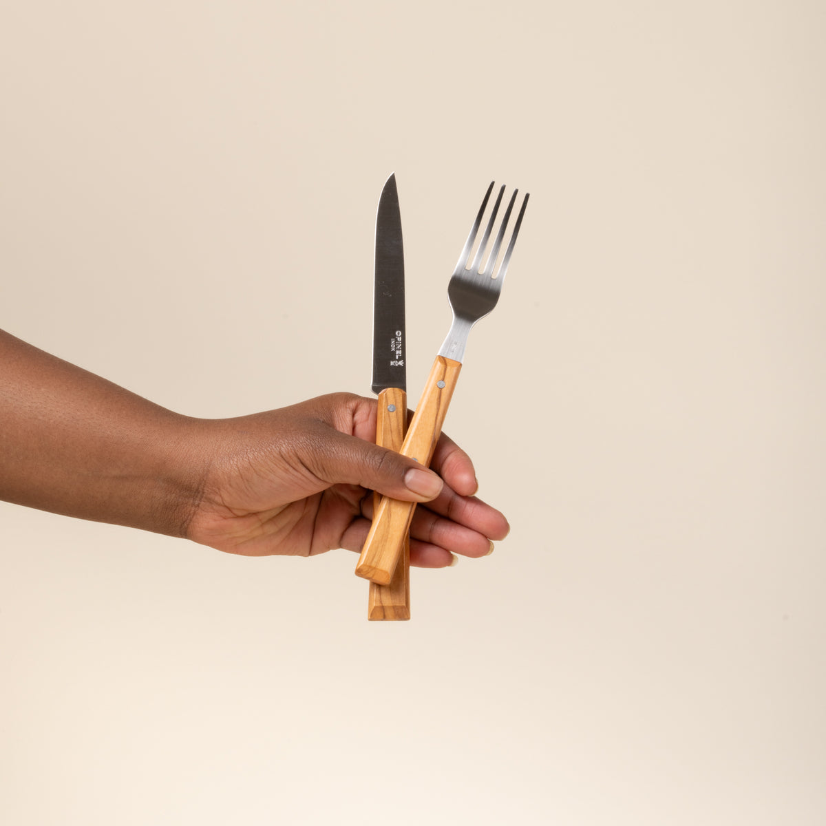 A hand holds out a Opinel table knife and fork with wooden handles.