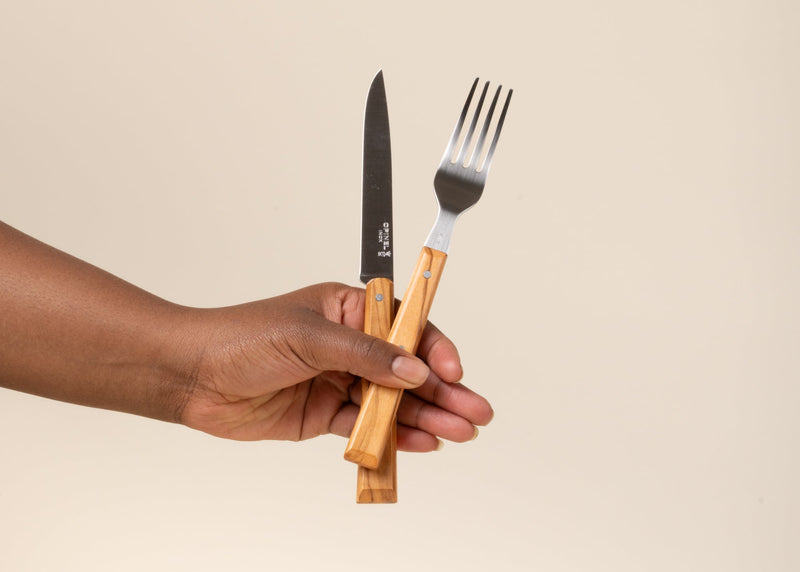 A hand holds out a Opinel table knife and fork with wooden handles.