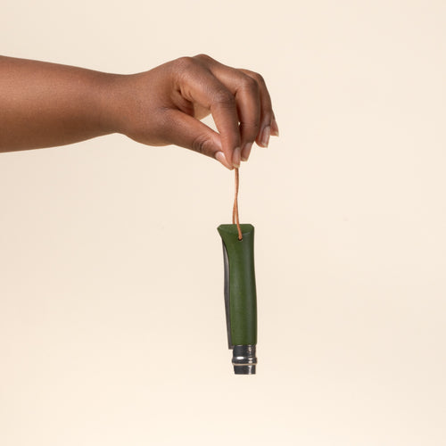 A hand holds a green-handled folded knife with stainless steel blade and leather lanyard.