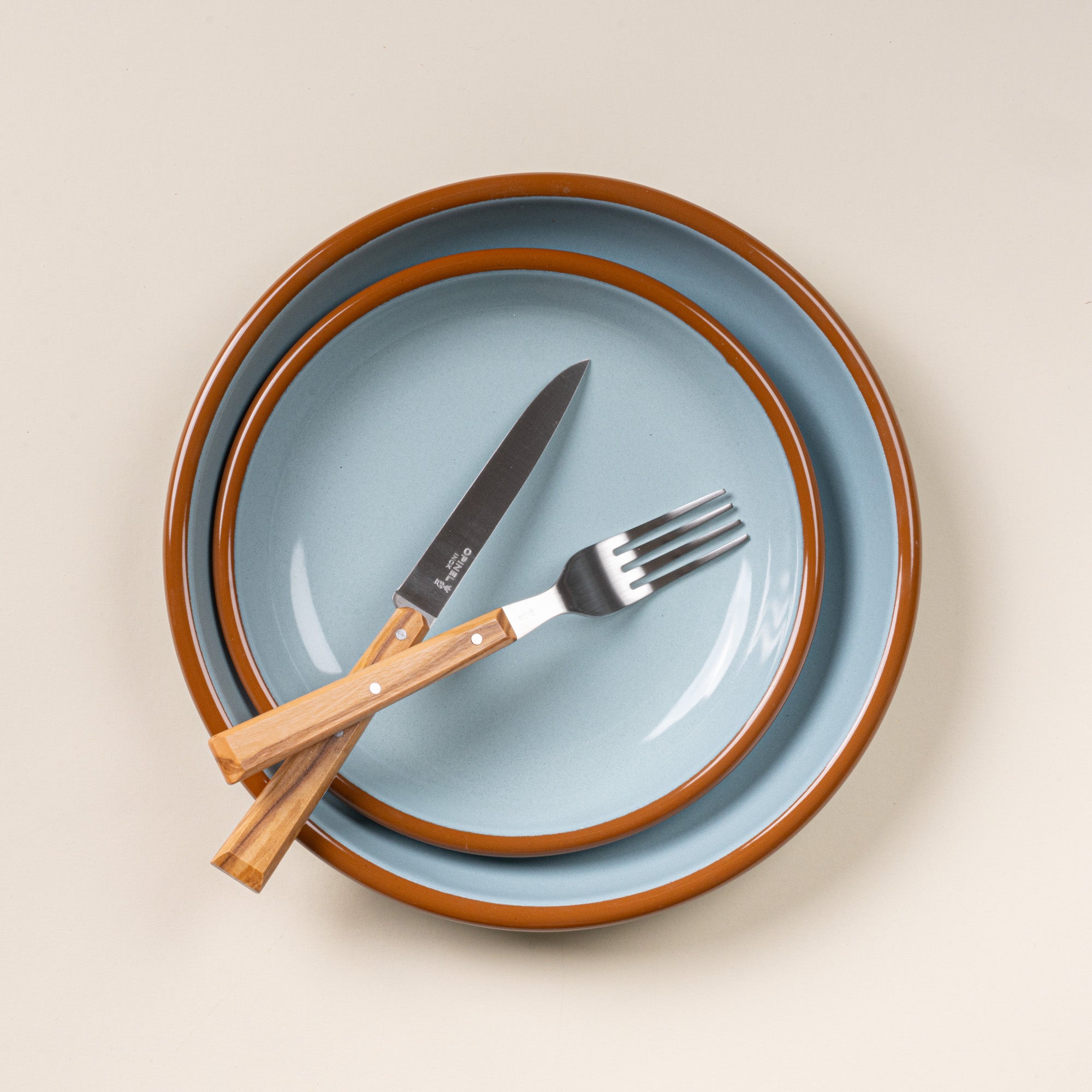 Opinel table knife and fork with wooden handles sitting on enamel plates and bowls in robin's egg blue.