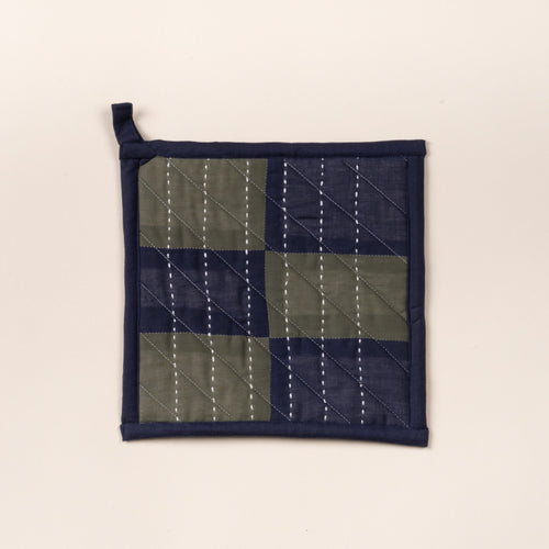 Quilted pot holder with green and navy patchwork squares and white stitched lines, with hanging loop.