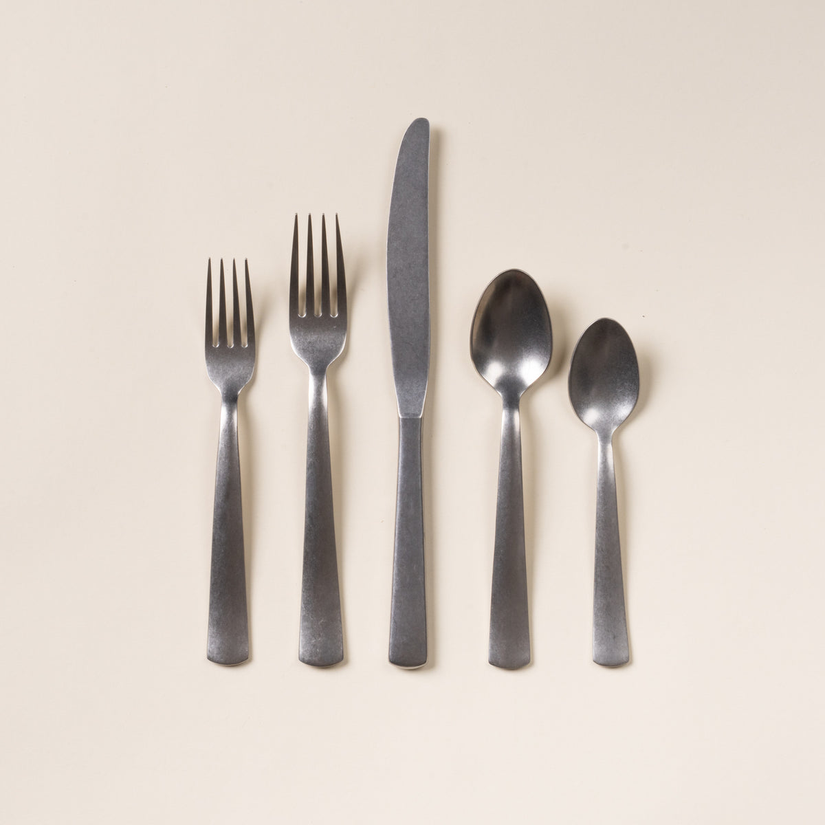 Five matte stainless steel utensils—salad fork, dinner fork, knife, tablespoon, and teaspoon—arranged on a neutral background.