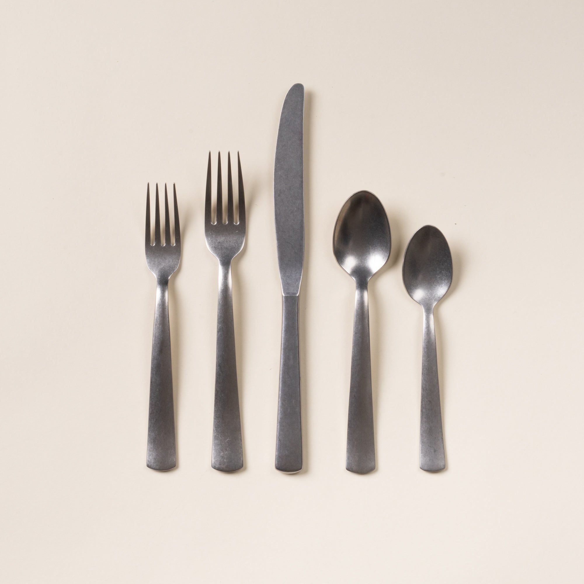 Five matte stainless steel utensils—salad fork, dinner fork, knife, tablespoon, and teaspoon—arranged on a neutral background.
