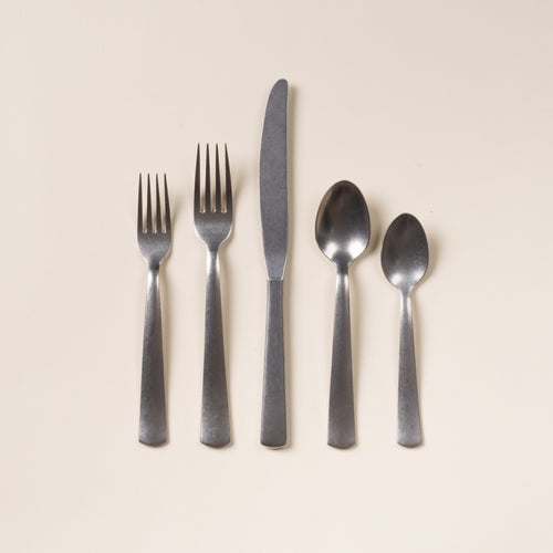 Five matte stainless steel utensils—salad fork, dinner fork, knife, tablespoon, and teaspoon—arranged on a neutral background.