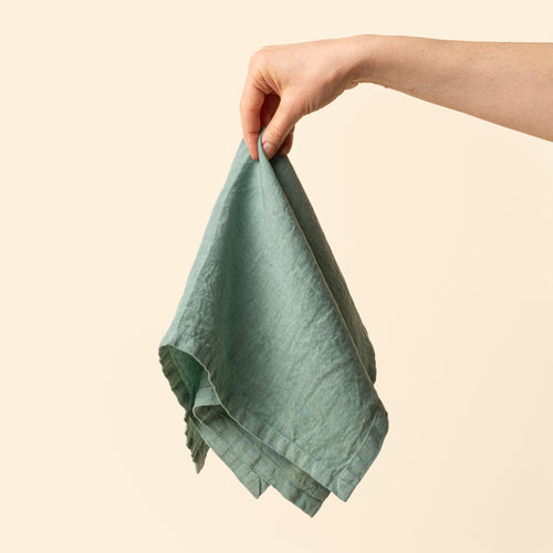 A hand holds out a linen napkin in a green color