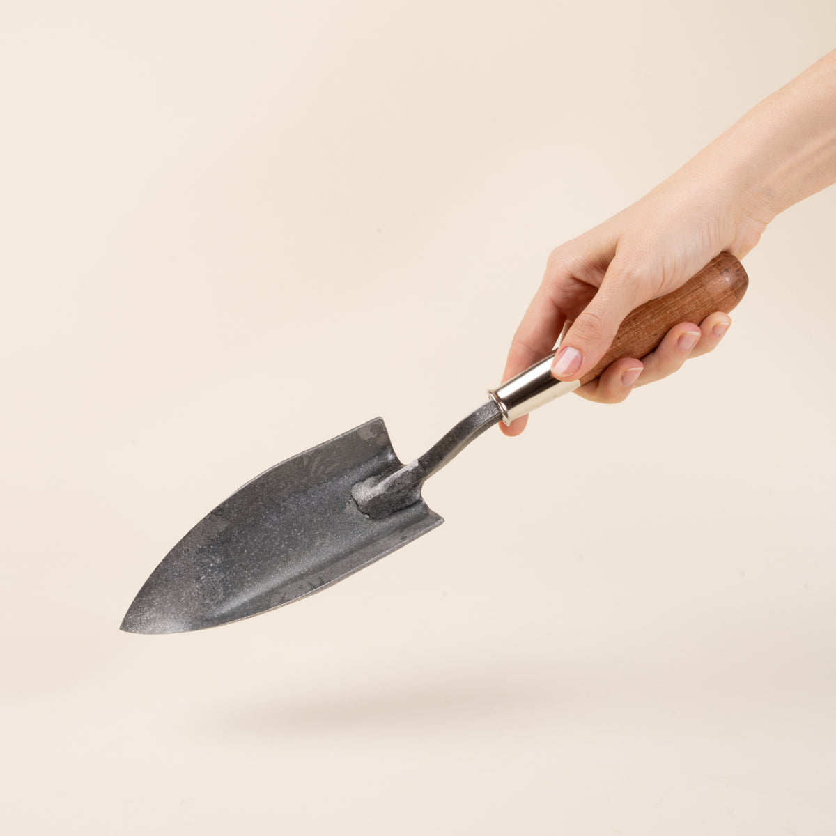 A hand holds a garden trowel with a pointed blade and wooden handle.