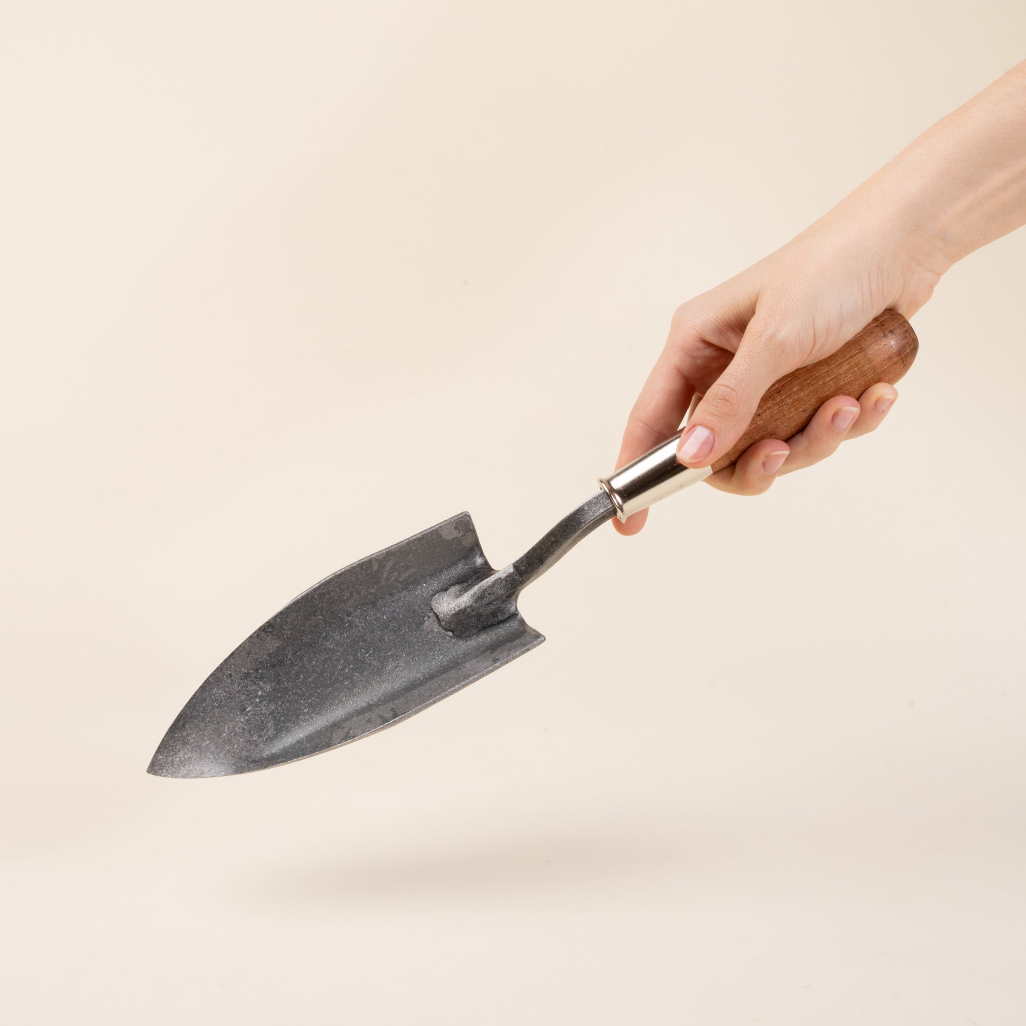 A hand holds a garden trowel with a pointed blade and wooden handle.