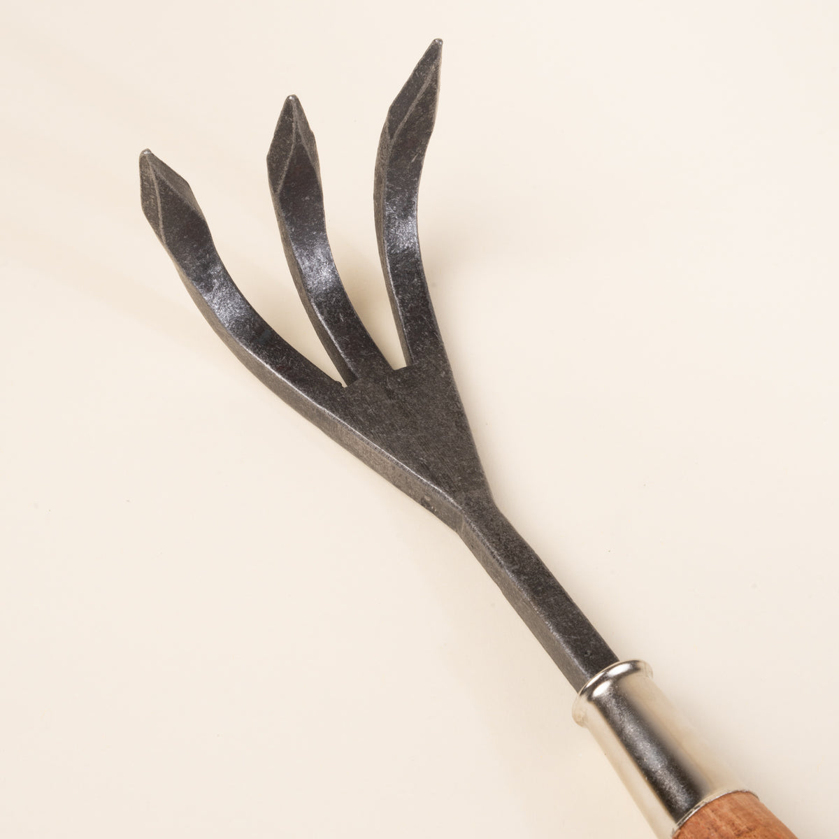 A closeup of a three-prong garden cultivator with a wooden handle.