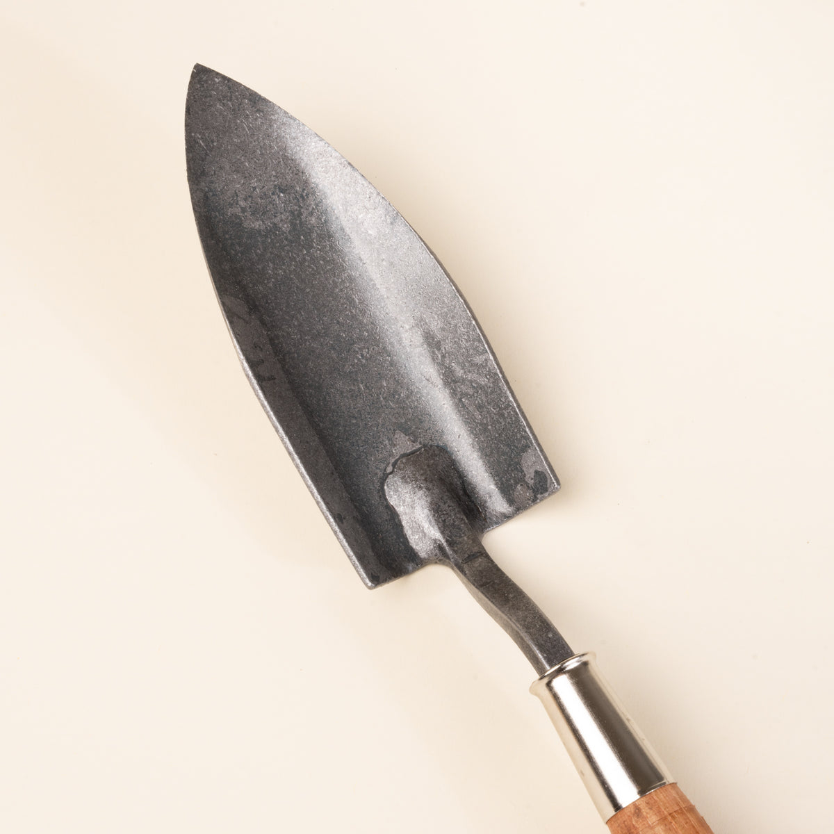A closeup of a garden trowel with a pointed blade and wooden handle.