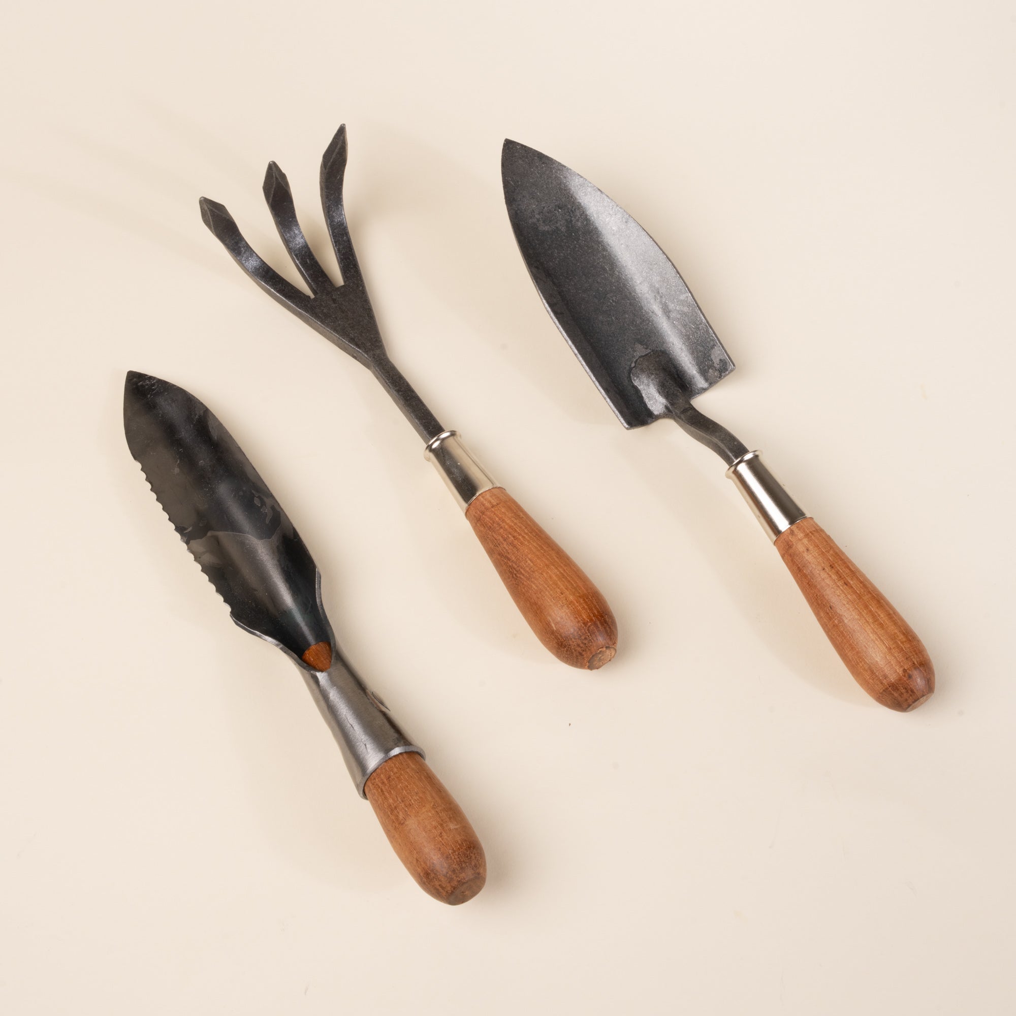 Three hand garden tools with wooden handles: a trowel, fork cultivator, and serrated transplanting tool.