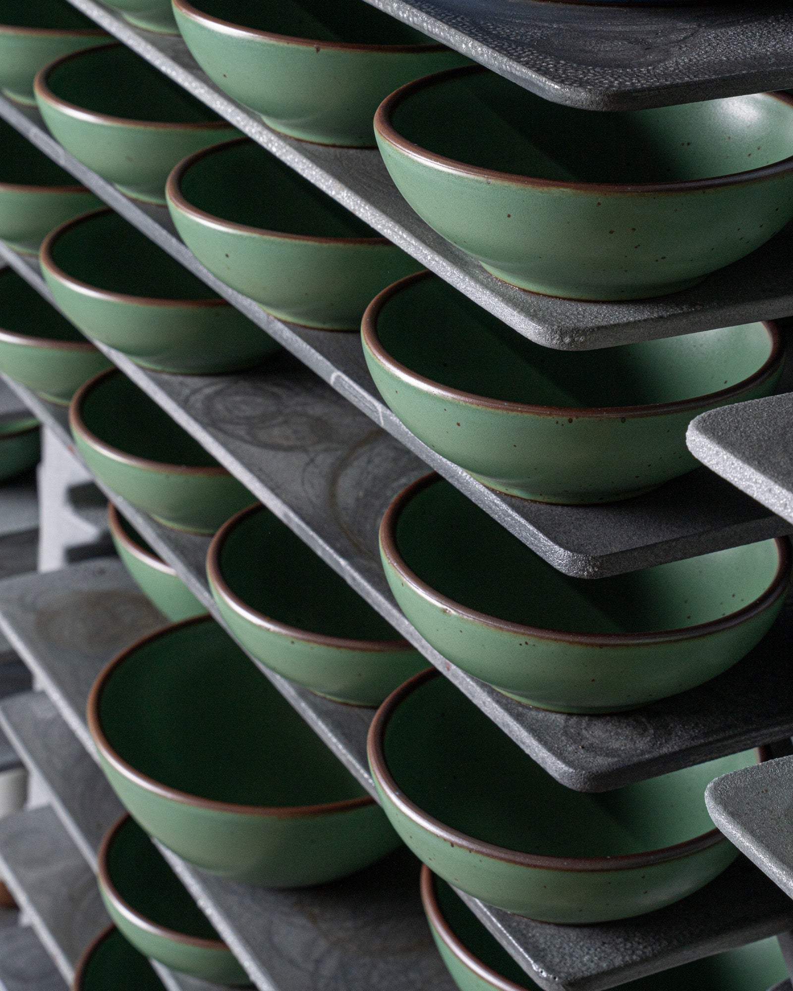 Stack of green ceramic bowls on a gray metal shelf