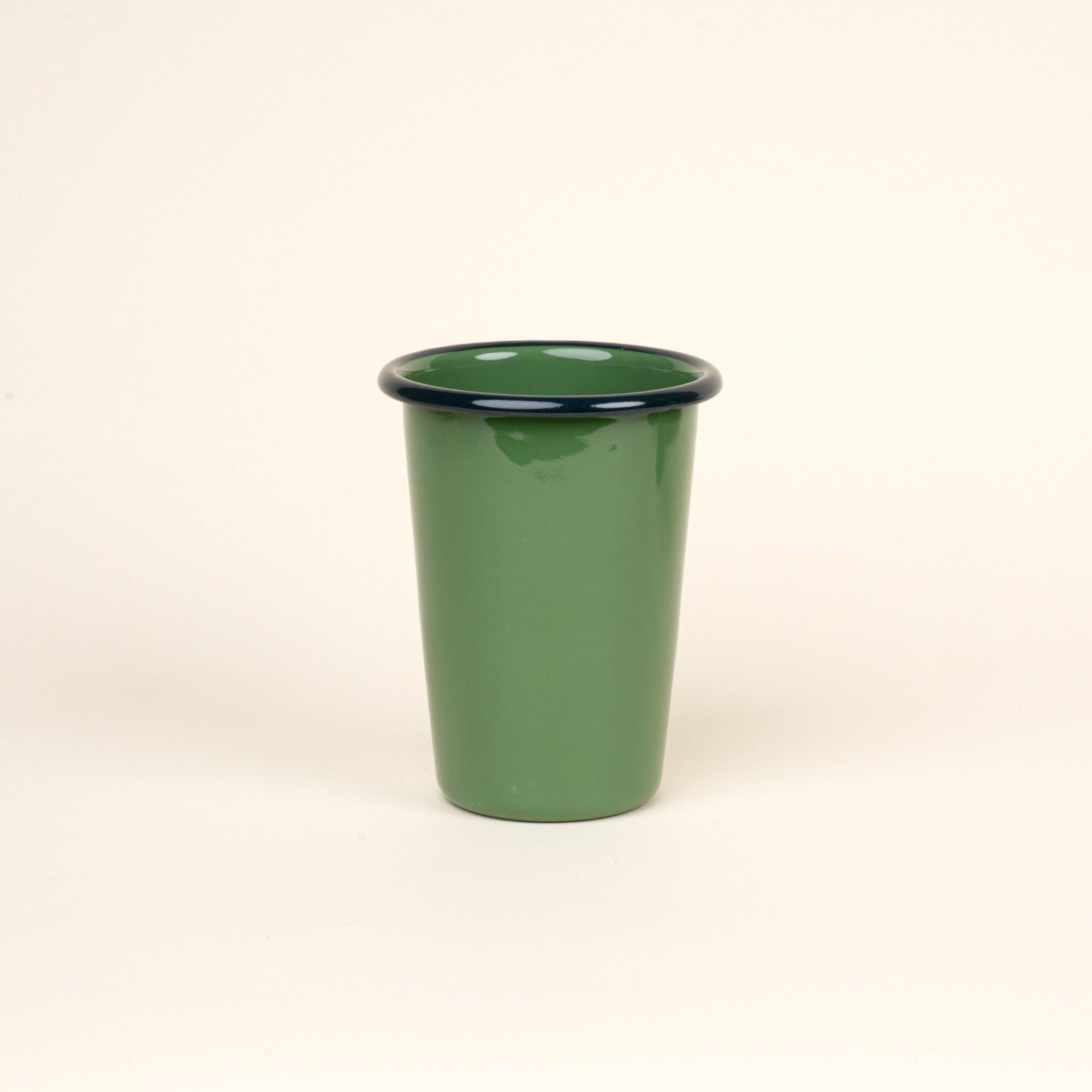 A tall green enamel tumbler with a dark rim, set against a soft beige background.