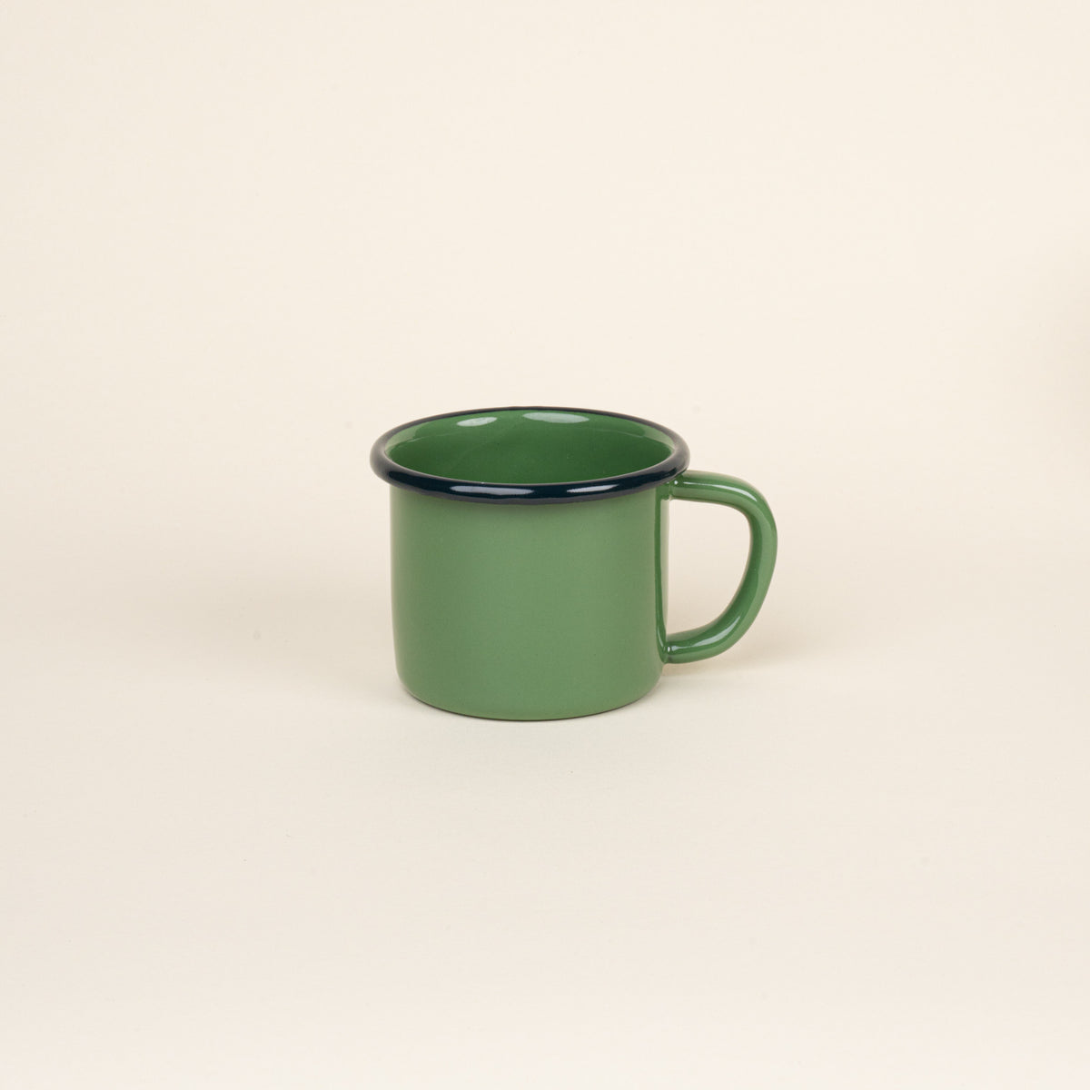 A green enamel mug with a dark rim and handle, shown against a neutral beige background.