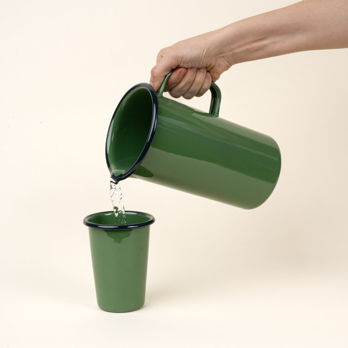 Green enamel pitcher pouring water into another green cup on a beige background