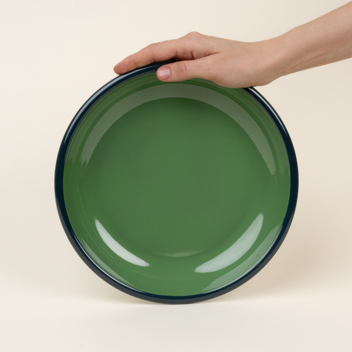 A hand props up an enamel dinner plate in green with an dark rim.