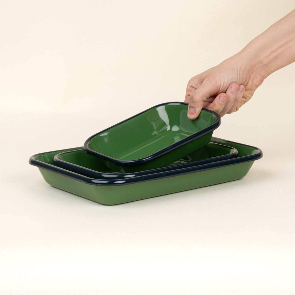 A hand placing a small dish into a nesting trio rectangular baking dishes in a green color with a dark green rim.