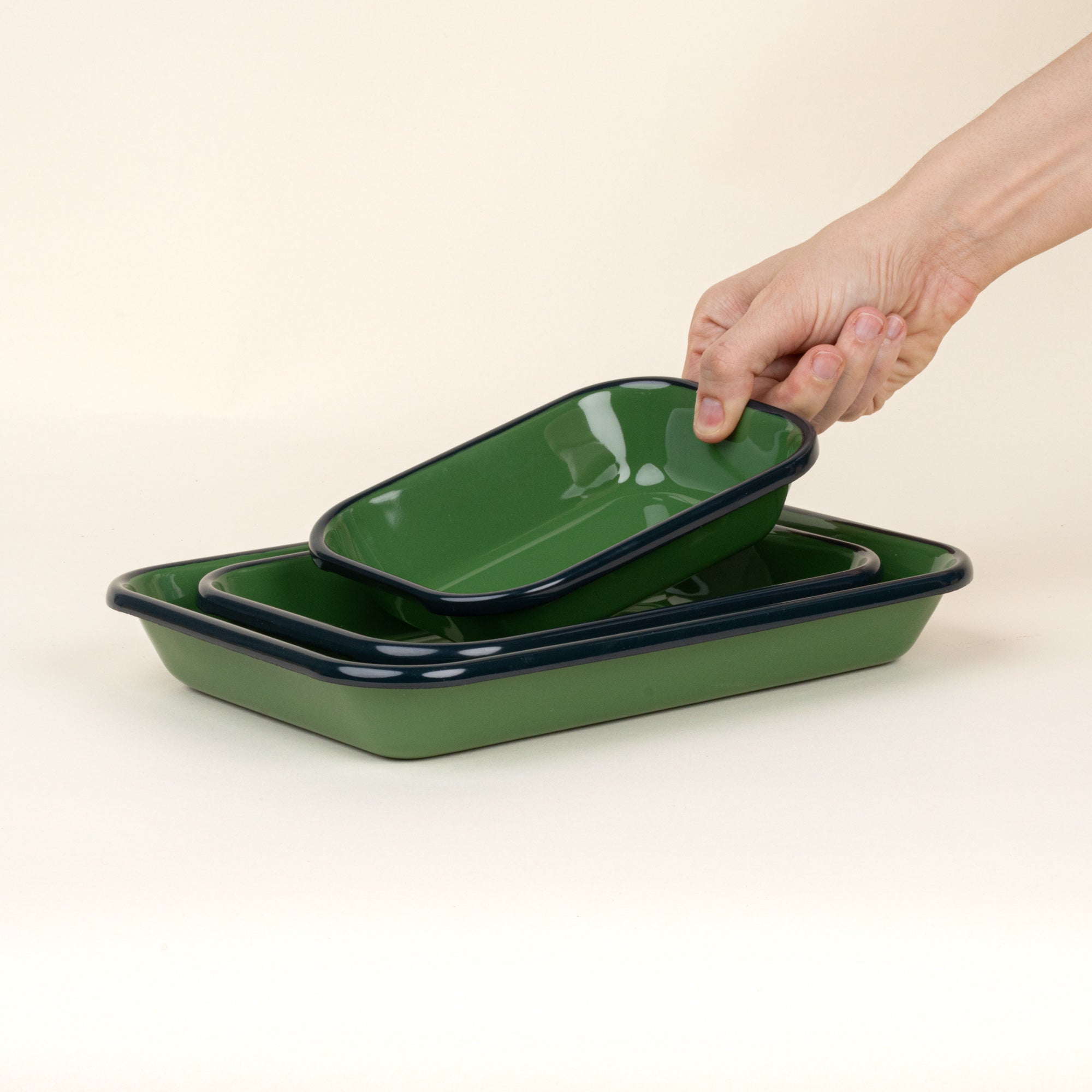 A hand placing a small dish into a nesting trio rectangular baking dishes in a green color with a dark green rim.