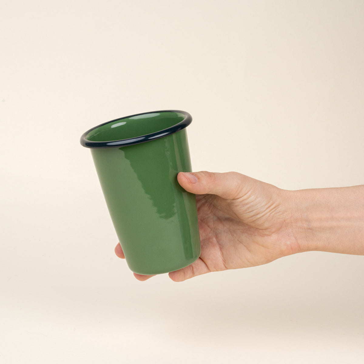 Hand holding a tall green enamel tumbler with a dark rim