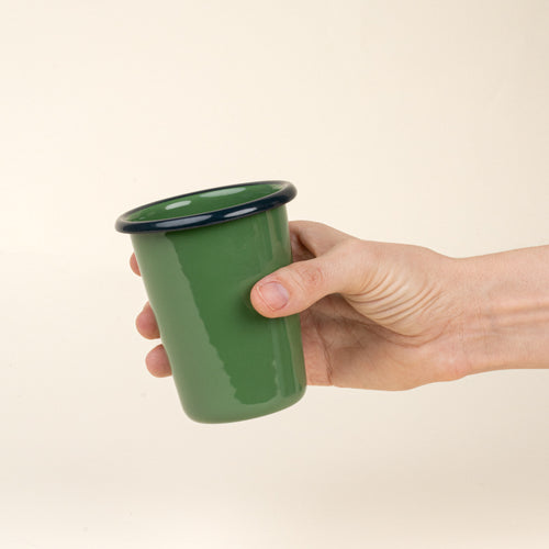 Hand holding a short green enamel tumbler with a dark rim