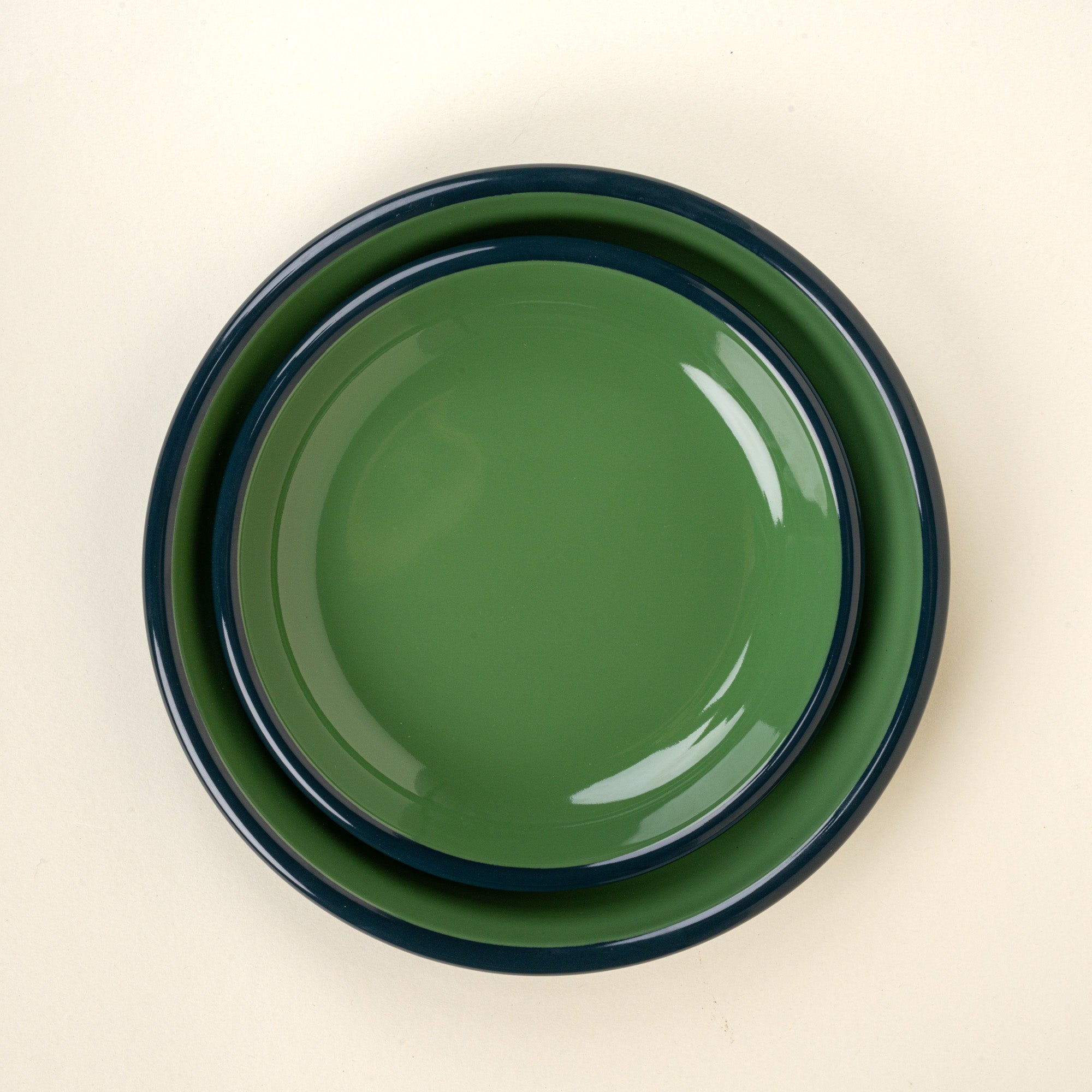 A nesting enamel side plate and dinner plate in green with a dark rim.