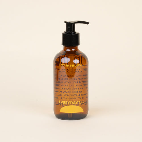 Brown bottle with pump titled 'Warm Feelings Everyday Oil' on a beige background