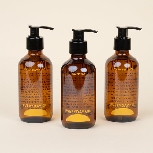 Three bottles of Everyday Oil with pump dispensers on a beige background