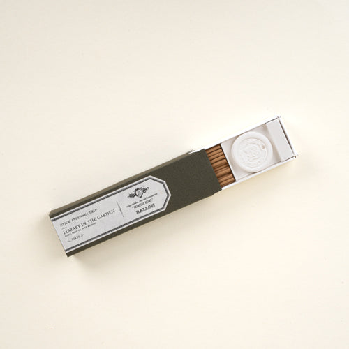 Open box of stick incense labeled “Library in the Garden,” showing incense sticks and a small holder on a neutral background.