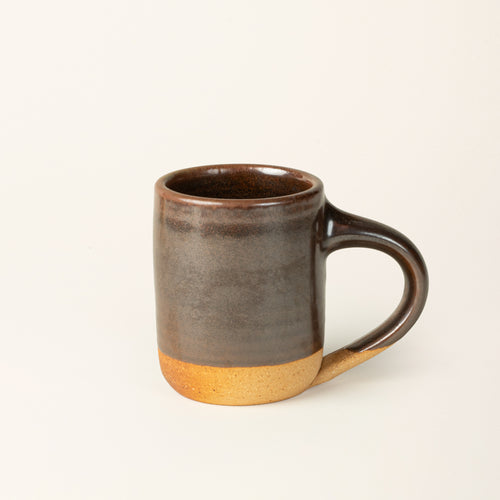 A handmade ceramic mug with a wood fired earthy muddy glaze with an unglazed base.