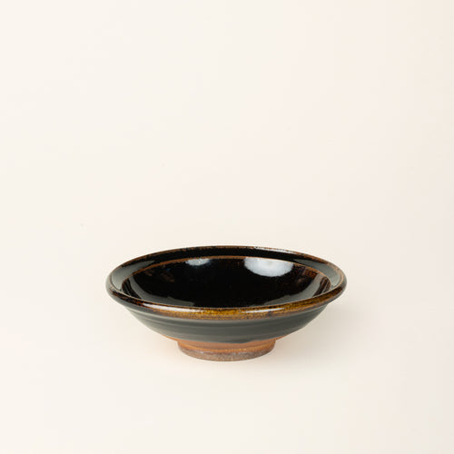 A small handmade ceramic bowl with a wood fired earthy muddy glaze and an unglazed base.
