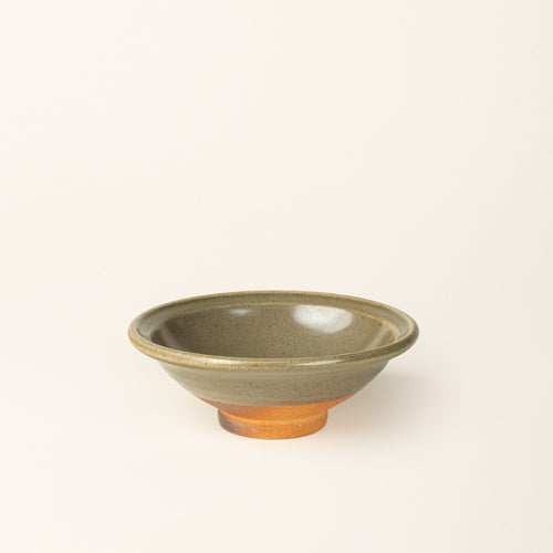 A small handmade ceramic bowl with a wood fired light earthy green glaze and an unglazed base.