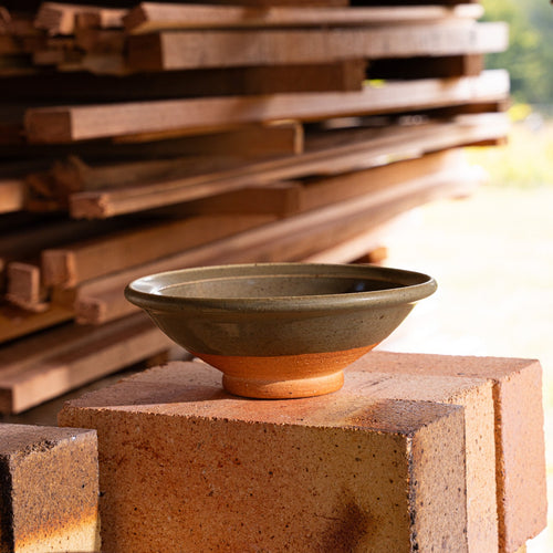 A handmade ceramic bowl with a wood fired light earthy green glaze and an unglazed base, in a kiln.