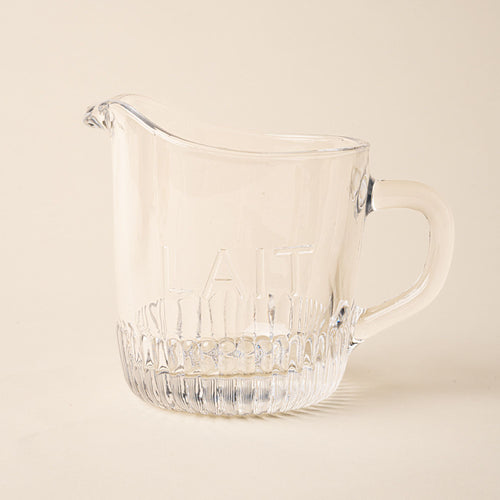 Clear glass pitcher with handle and spout on a light background