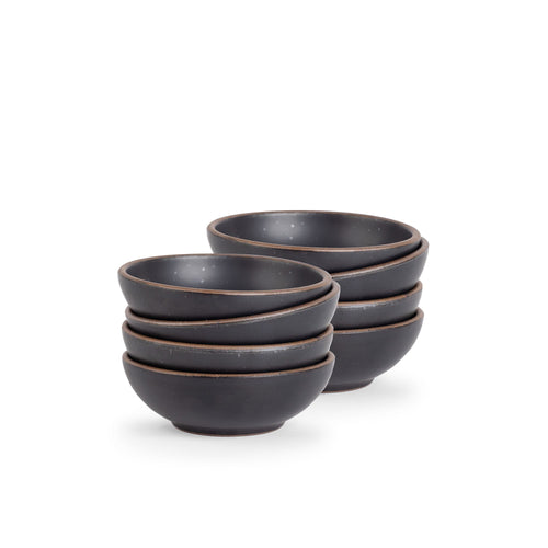 A stack of 8 small shallow ceramic bowls in a graphite black color featuring iron speckles and an unglazed rim