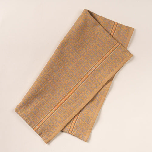 Muted gold woven kitchen towel with a subtle textured pattern and slim striped accent, folded neatly on a clean neutral background.