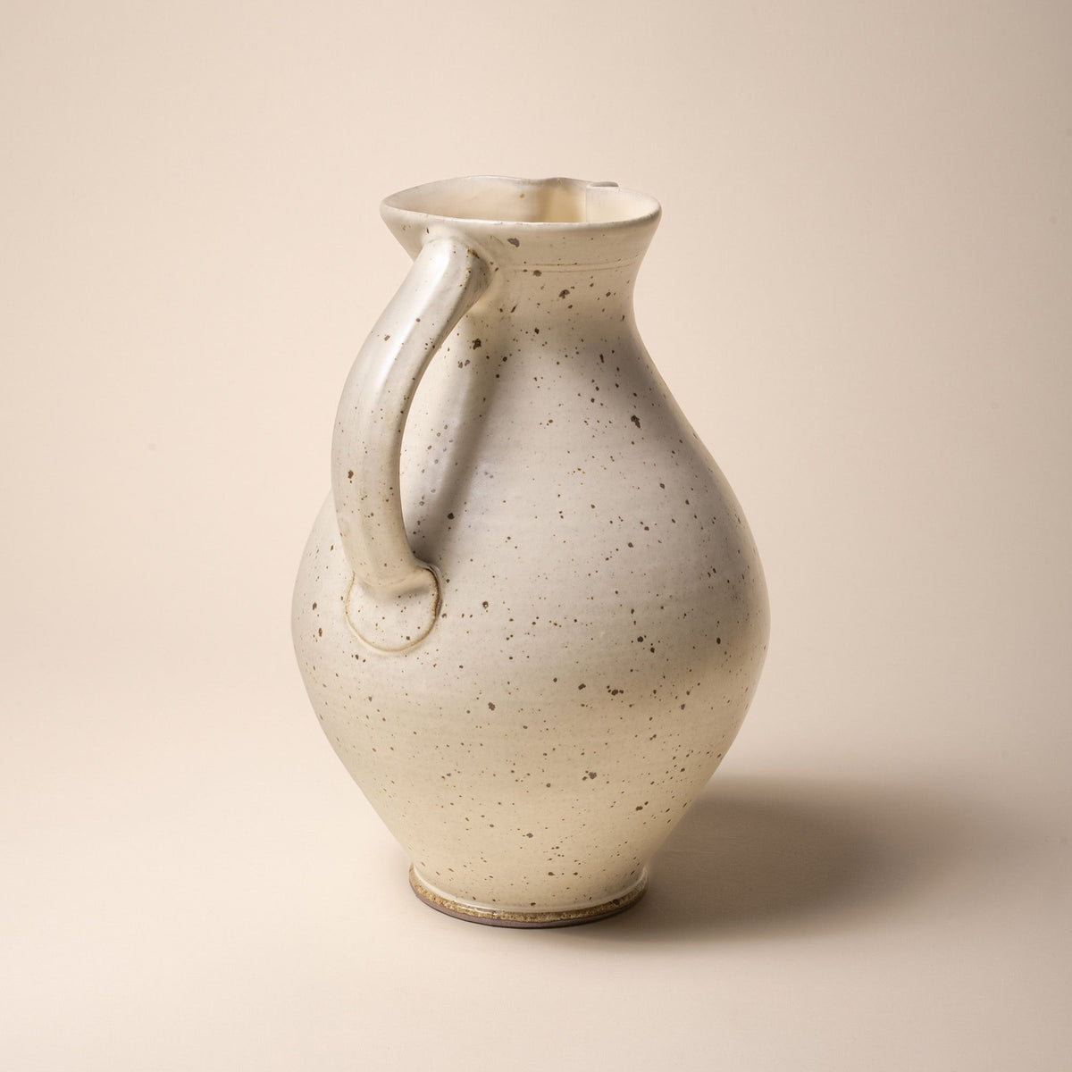 A hand-formed large classic ceramic pitcher with a spout and handle in a warm off-white color with iron speckles